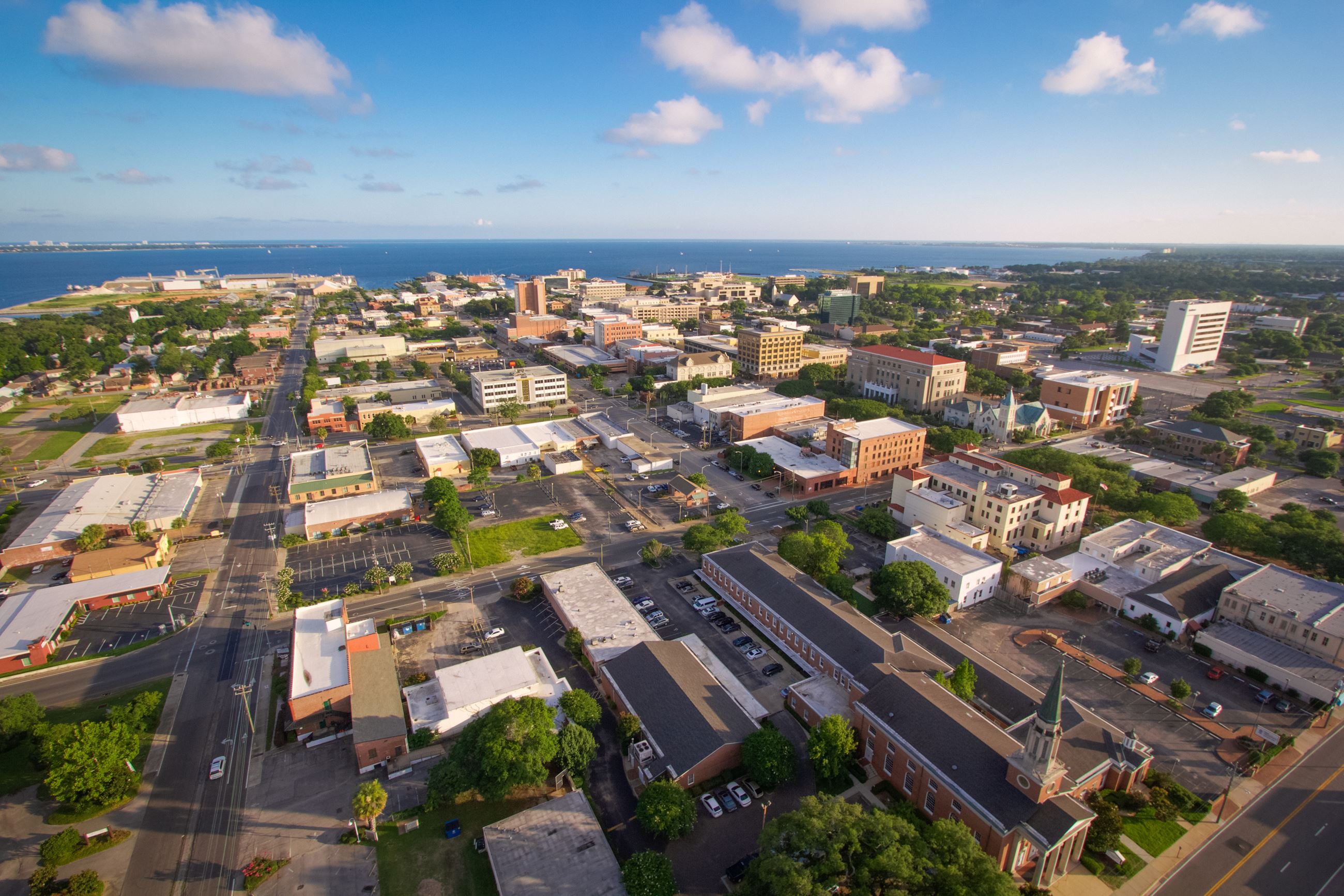 Aerial of businesses and buildings in downtown Pensacola with bay in background