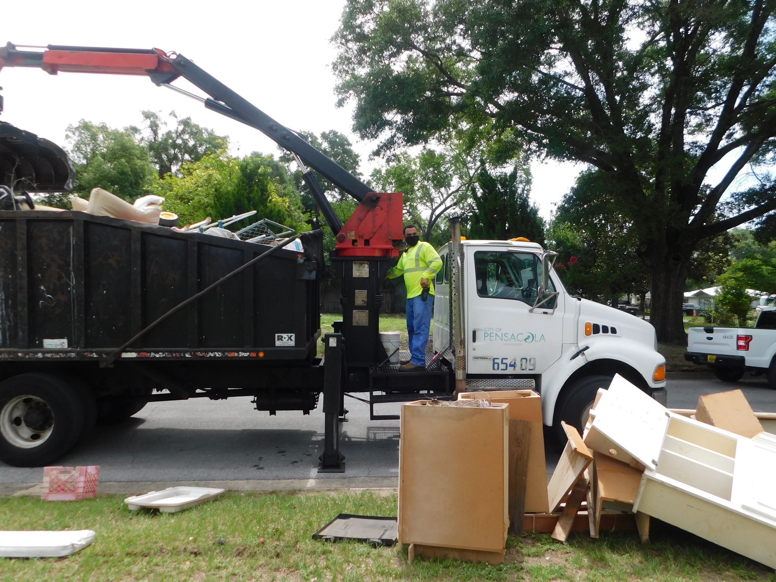 A city sanitation worker on a truck picks up debris during the mayor's neighborhood cleanup